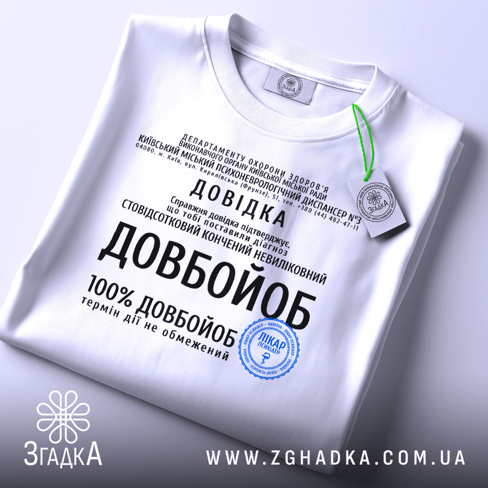Футболка довідка довбойоб подарунок, біла футболка, розкладена на поверхні, з принтом чорного кольору, фон світло-сірий, на футболці є етикетка з зеленим шнурком.