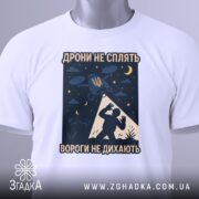 Футболка дрони не сплять, біла, зображена на манекені, фон світло-сірий, принт з дронами, українським гербом та силуетом людини, деталі принта чітко видимі.