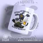 Футболка дрони працюють подарунок. Чашка білого кольору з глянцевою поверхнею, зображення дрону та танка на передній частині. Принт містить напис 'Дрони працюють - вороги мовчать!' та елементи графіки, такі як вибухи та дим. Ручка чашки класична, з округлою формою, край чашки гладкий.
