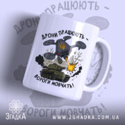 Футболка дрони працюють подарунок. Чашка білого кольору з глянцевою поверхнею, зображення дрону та танка на передній частині. Принт містить напис 'Дрони працюють - вороги мовчать!' та елементи графіки, такі як вибухи та дим. Ручка чашки класична, з округлою формою, край чашки гладкий.