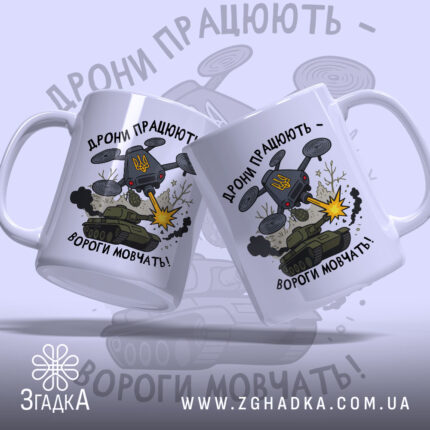Футболка дрони працюють подарунок. Дві чашки білого кольору з глянцевою поверхнею, розташовані під кутом один до одного. Принт на обох чашках однаковий, з написом 'Дрони працюють - вороги мовчать!' та ілюстрацією дрону, що стріляє. Ручки чашок класичні, з округлою формою, краї гладкі.