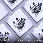 Футболка динозавр без фільтрів, біла, складена в хаотичному порядку з іншими футболками, фон світло-сірий, принт з чорним малюнком динозавра на драбині та текстом.