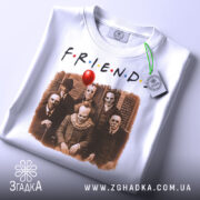 Футболка friends жахи подарунок, біла, складена на столі, фон світлий, принт з персонажами жахів, на етикетці зелена стрічка.