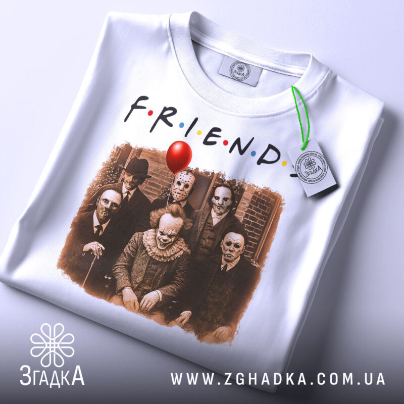 Футболка friends жахи подарунок, біла, складена на столі, фон світлий, принт з персонажами жахів, на етикетці зелена стрічка.