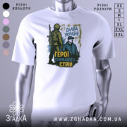 Футболка герої тримають стрій. Біла футболка з принтом, на якому зображені два чоловіки: один у військовій формі, інший у цивільному одязі. Принт виконаний у темно-зелених та жовтих тонах, на фоні видно напис 'Слава Україні'.