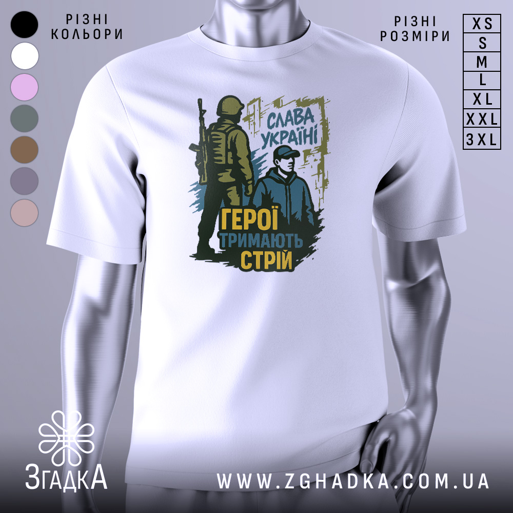 Футболка герої тримають стрій. Біла футболка з принтом, на якому зображені два чоловіки: один у військовій формі, інший у цивільному одязі. Принт виконаний у темно-зелених та жовтих тонах, на фоні видно напис 'Слава Україні'.