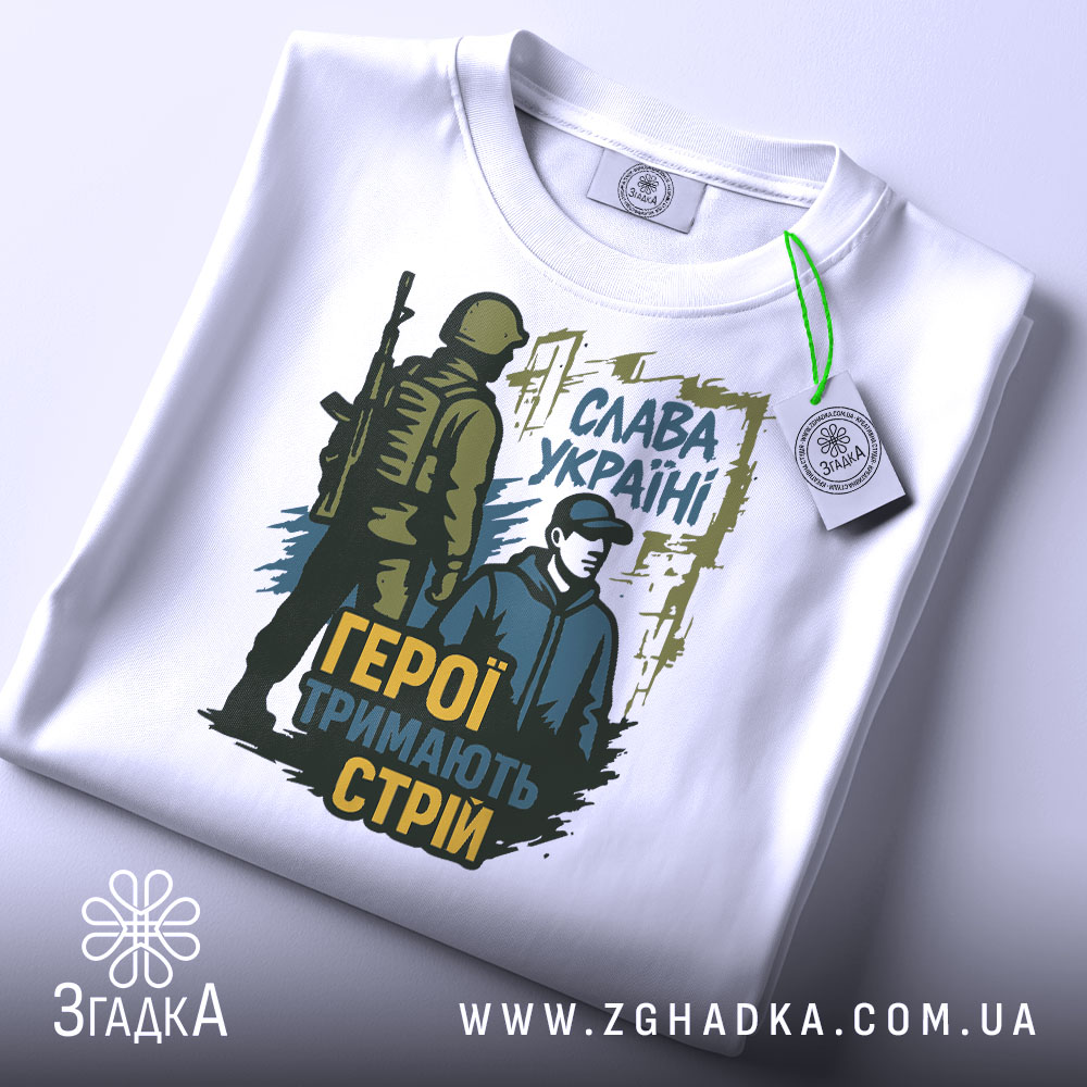 Футболка герої тримають стрій. Біла футболка, на якій зображено той же принт, але з видимим етикеткою на комірці. Принт яскравий, з акцентом на військову тематику та патріотичний зміст.