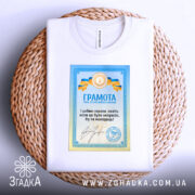 Футболка грамота з написом, білого кольору, зображена на кошику, фон натурального кольору, принт з грамотою у блакитних та жовтих кольорах, текст на українській мові.