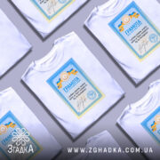Футболка грамота з написом, білого кольору, зображена на фоні сірого кольору, кілька складених футболок, принт з грамотою у блакитних та жовтих кольорах, текст на українській мові.