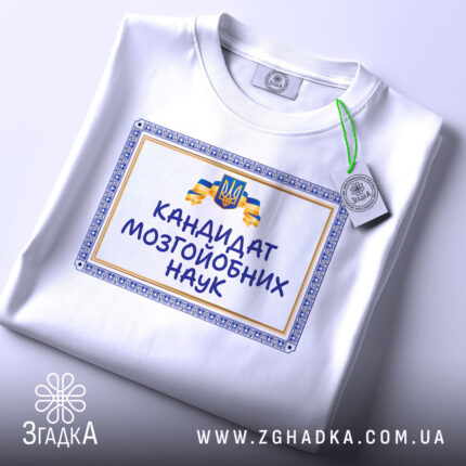 Футболка кандидат мозгойобних наук, біла, складена на столі, фон світло-сірий, принт з написом "КАНДИДАТ МОЗГЙОБНИХ НАУК" в обрамленні, з зеленим ярликом.