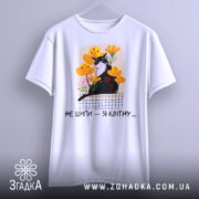 Футболка кіт не шипи, білого кольору, підвішена на вішалці, фон світло-сірий, принт з чорним котом на фоні жовтих і рожевих квітів, текст під принтом чорний.