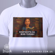 Футболка книгонута на всю голову, білого кольору, з ракурсу спереду, на фоні розмитого сірого кольору, з принтом, що зображує дівчину з книгою на фоні книжкових полиць.