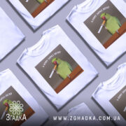 Футболка кому зараз легко, біла, зображена зверху на кількох футболках, фон сірий, принт з папугою, що тримає сигарету, текст зверху: 'А КОМУ ЗАРАЗ ЛЕГКО'.