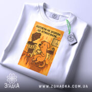 Футболка котлети не згоріли. Біла толстовка з принтом, на якому зображений жовтий собака, що сидить на стільці з чашкою в руках. На фоні видно кухонну плиту з димом та вогнем. Футболка зображена зверху, з етикеткою, що звисає.