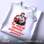 Футболка маєш право відрізнятись. Білий колір, зображена зверху, фон світлий, принт з червоним текстом і чорною ілюстрацією жінки, на футболці є етикетка.