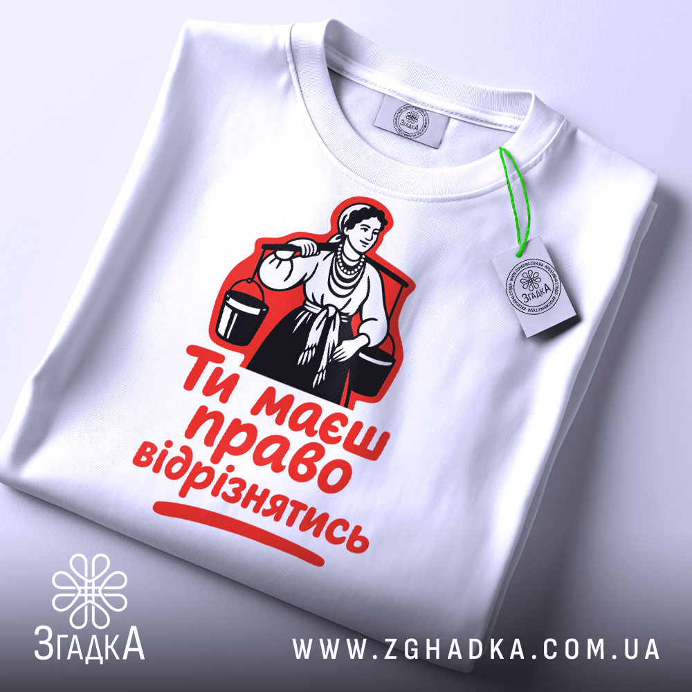 Футболка маєш право відрізнятись. Білий колір, зображена зверху, фон світлий, принт з червоним текстом і чорною ілюстрацією жінки, на футболці є етикетка.