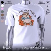 Футболка моє пузо гордість. Біла футболка з принтом кота, що сидить на дивані, з ракурсу спереду. Фон світло-сірий, принт кольоровий, котик у блакитній футболці з усмішкою і піднятою рукою.