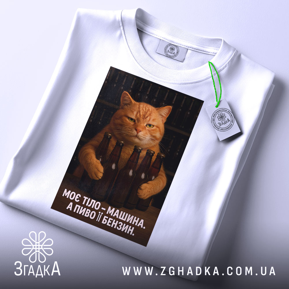 Футболка моє тіло машина. Біла футболка, складена на поверхні, з принтом кота, що тримає пляшки пива. На футболці є етикетка з зеленим шнурком. Фон світлий, що підкреслює деталі принта.