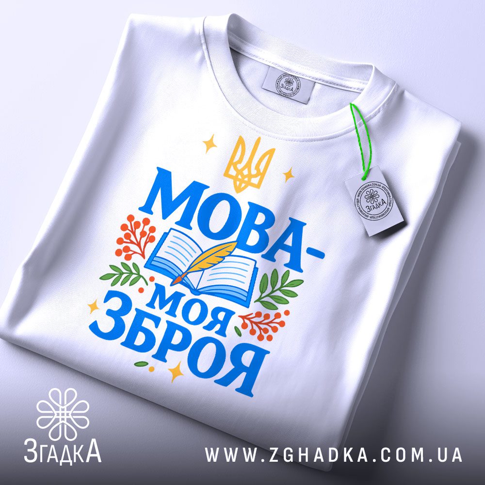Футболка Мова моя зброя, білого кольору, зображена зверху на плоскій поверхні, фон світло-сірий, принт з синім текстом "МОВА-МОЯ ЗБРОЯ" та елементами книжки, пера і рослин, з етикеткою на комірці.