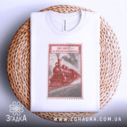 Футболка на повній швидкості, біла, з ракурсу зверху, на фоні плетеного кошика, принт з паровозом в червоному кольорі, оформлений як поштовий штамп.