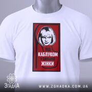 Футболка напис під каблуком, біла, зображена на манекені, фон світло-сірий, принт червоний з чорною обводкою, на якому зображена жінка з коротким волоссям та написом 'ПІД КАБЛУКОМ У СИЛЬНОЇ ЖІНКИ'.
