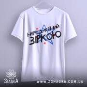 Футболка народжений зіркою подарунок, біла, підвішена на вішалці, фон однотонний, принт містить текст "НАРОДЖЕНИЙ ЗІРКОЮ" з червоними і синіми зірками.