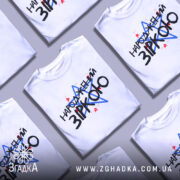 Футболка народжений зіркою подарунок, біла, складена на столі, фон однотонний, принт містить текст "НАРОДЖЕНИЙ ЗІРКОЮ" з червоними і синіми зірками, кілька футболок розкладені поряд.