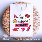 Футболка не чіпай розтану, біла, складена на плетеній кошику, фон білий, принт з червоними туфлями, губами, жовтими зірочками та текстом.