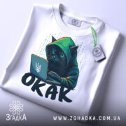 Футболка окак мем подарунок, біла футболка, складена в квадрат, з принтом чорного кота в капюшоні, який працює за ноутбуком, на фоні світло-сірого кольору, з етикеткою зеленого кольору.