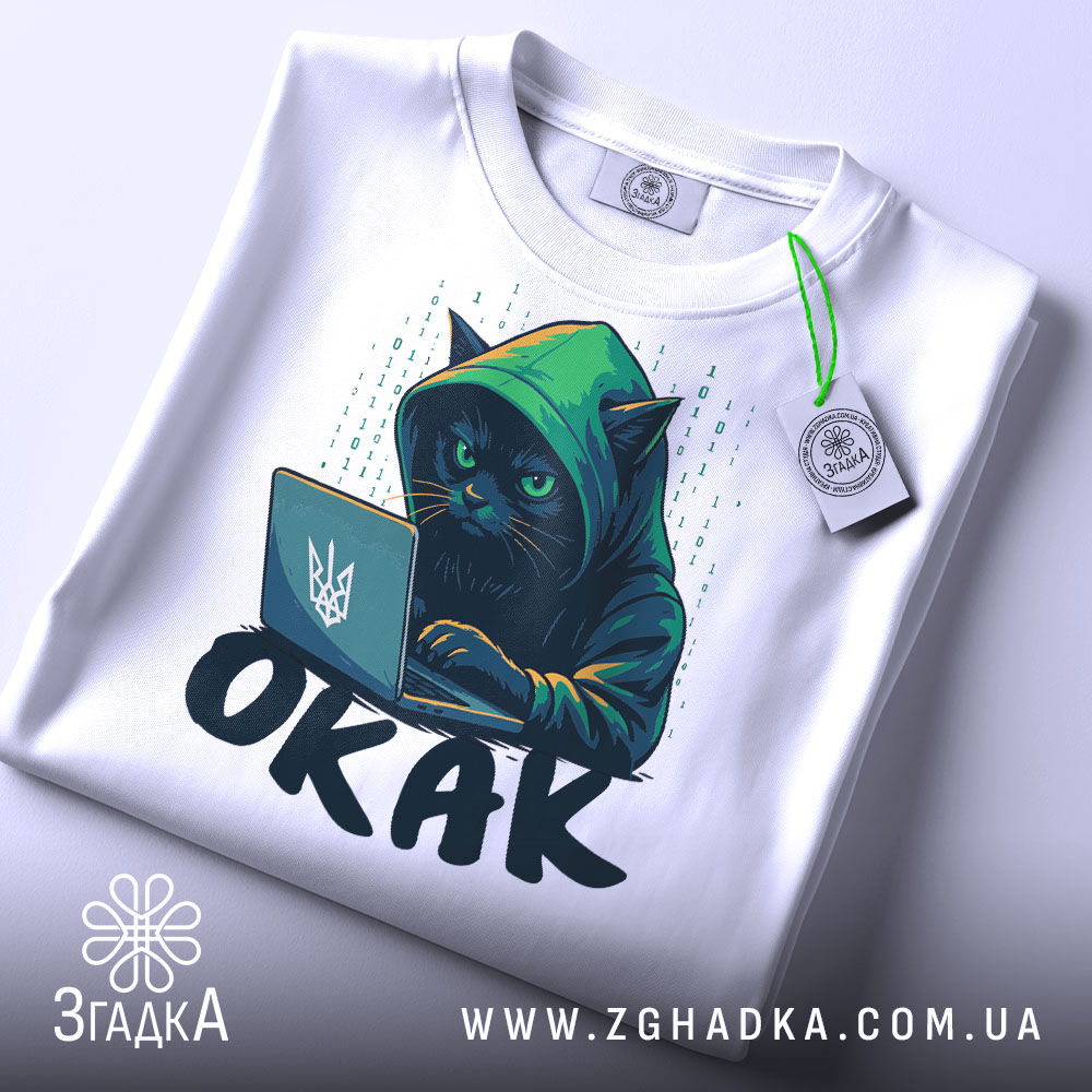 Футболка окак мем подарунок, біла футболка, складена в квадрат, з принтом чорного кота в капюшоні, який працює за ноутбуком, на фоні світло-сірого кольору, з етикеткою зеленого кольору.