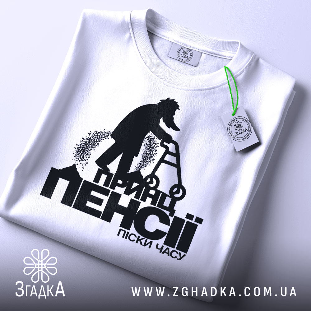 Футболка принц пенсії піски. Біла футболка, складена на поверхні, принт на видимій частині, фон світлий, деталі принта чітко видимі, з етикеткою на комірці.