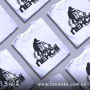 Футболка принц пенсії піски. Біла футболка, розкладена на поверхні, фон світло-сірий, принт чорного кольору, зображення чоловіка на ходунках, кілька футболок в кадрі.