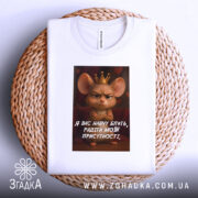 Футболка радіти моїй присутності, біла, зображена на плоскій поверхні на кошику, фон світлий, принт з мишкою в короні та текстом на українській мові.