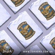 Футболка рибалка на воді, біла, складена на столі, фон сірий, кілька футболок з принтом рибалки на човні.