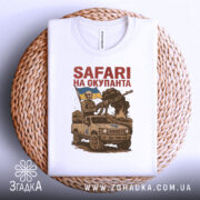 Футболка сафарі на окупанта, біла, зображена з верхнього ракурсу на плетеному кошику, фон світло-сірий, принт з військовим у шоломі, що тримає гвинтівку, та автомобілем з українським прапором.