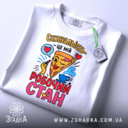 Футболка сексуальність робочий стан, біла футболка з кольоровим принтом, ракурс зверху, фон світлий, принт з піцою та серцями, етикетка з зеленим шнурком.