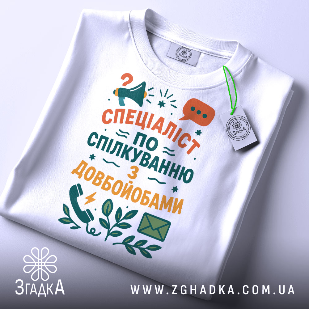 Футболка спілкування з довбойобами, білого кольору, складена на поверхні, фон світло-сірий, принт з текстом "СПЕЦІАЛІСТ ПО СПІЛКУВАННЮ З ДОВБОЙОБАМИ" в яскравих кольорах, з елементами мегафона та листа, на футболці є етикетка.