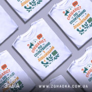 Футболка спілкування з довбойобами, білого кольору, складена на поверхні, фон світло-сірий, принт з текстом "СПЕЦІАЛІСТ ПО СПІЛКУВАННЮ З ДОВБОЙОБАМИ" в яскравих кольорах, з елементами мегафона та листа, кілька футболок розташовані поруч.