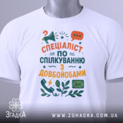 Футболка спілкування з довбойобами, білого кольору, зображена на манекені, фон світло-сірий, принт містить текст "СПЕЦІАЛІСТ ПО СПІЛКУВАННЮ З ДОВБОЙОБАМИ" в яскравих кольорах, з іконками телефону та листа.