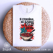 Футболка спокійна як борщ. Біла футболка, складена на плетеній основі, з принтом борщу, червоним фоном і чорним написом, виглядає затишно.