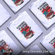 Футболка спокійна як борщ. Біла футболка, складена в кілька шарів, з принтом борщу, червоним фоном і чорним написом, розташована на світлому фоні.