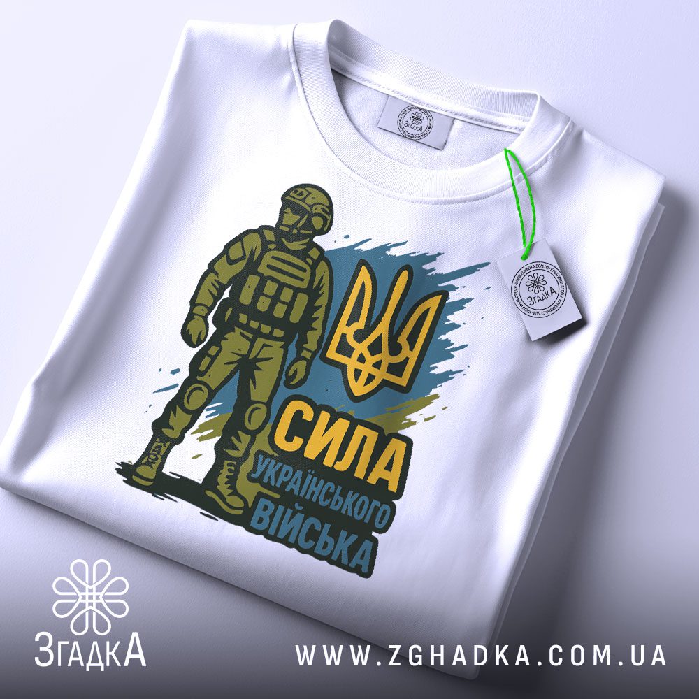 Футболка Сила українського війська, біла, розкладена на поверхні, фон світло-сірий, принт з воїном у формі та тризубом, присутня етикетка з зеленим кантом.