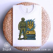 Футболка Сила українського війська, біла, складена на кошику з ротанга, фон білий, принт з воїном у формі та тризубом, акцент на текстурі кошика.