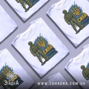 Футболка Сила українського війська, біла, розкладена на поверхні, фон світло-сірий, кілька футболок з однаковим принтом, акцент на повторюваності дизайну.