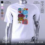 Футболка Тато супер герой, біла, зображена на манекені з правого боку, фон сірий, принт містить яскраві кольорові елементи з написами на українській мові.