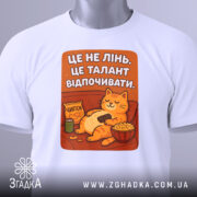 Футболка це не лінь. Біла футболка на манекені, з принтом кота, що відпочиває з чіпсами. Принт яскравий, текст на фоні оранжевого кольору.