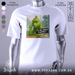 Футболка в дурку подарунок, біла футболка з принтом, на якому зображений зелений персонаж з сигаретою, ракурс спереду, фон - вікно з видом на природу.