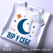 Футболка Вір у себе, біла, крупний план, принт з місяцем, зірками та кометою, фон світлий.