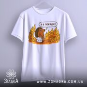 Футболка з їжаком в порядку. Біла футболка, підвішена на вішалці, з принтом їжака на унітазі. Принт яскравий, з оранжевими вогнями. Фон світлий, з легким градієнтом.