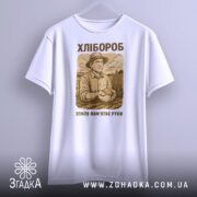 Футболка з малюнком хлібороба, білого кольору, зображена з фронтального ракурсу на світло-сірому фоні, принт з малюнком хлібороба в капелюсі, що тримає в руках землю, текст "ХЛІБОРОб" та "ЗЕМЛЯ ПАМ'ЯТАЄ РУКИ" в коричневих тонах.